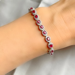 Könnte beinhalten: Ein silbernes Armband mit einer Reihe ovaler roter Edelsteine, die von kleineren, klaren Edelsteinen umgeben sind.