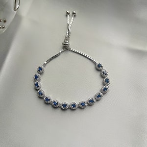 May include: A silver bracelet with a blue gemstone accent. The bracelet has a sliding knot closure.