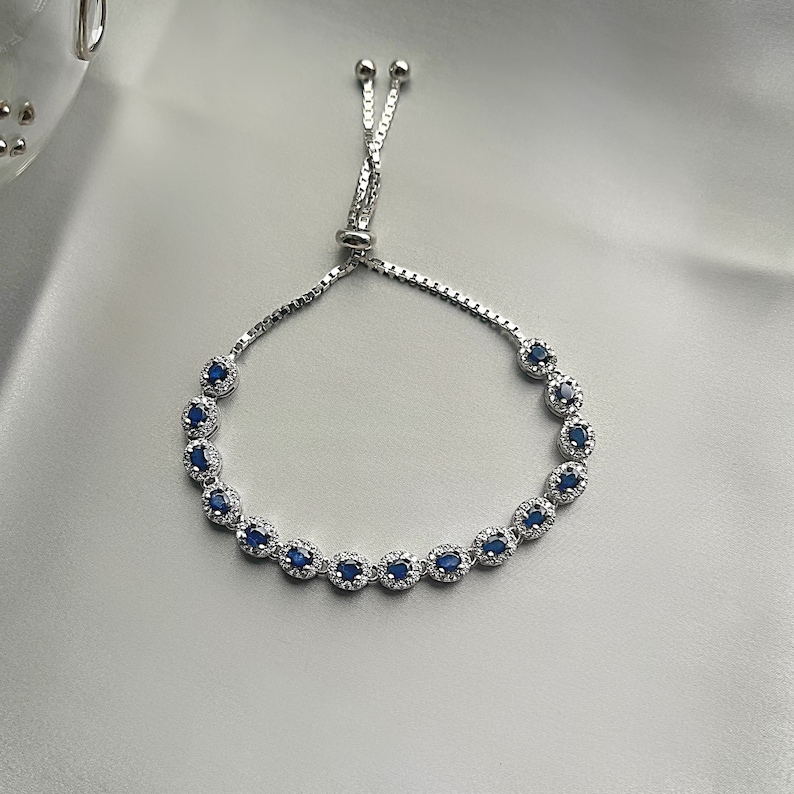 May include: A silver bracelet with a blue gemstone accent. The bracelet has a sliding knot closure.
