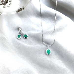 Puede incluir: Un collar y pendientes de plata con piedras preciosas verdes de forma ovalada rodeadas por un halo de piedras transparentes m&aacute;s peque&ntilde;as.
