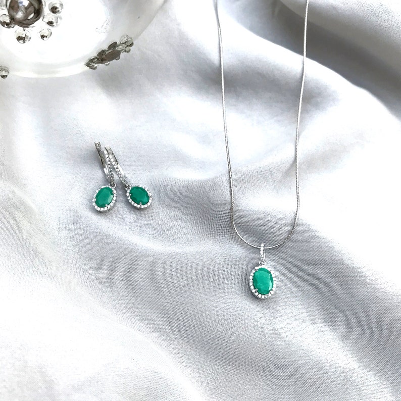 Puede incluir: Un collar y pendientes de plata con piedras preciosas verdes de forma ovalada rodeadas por un halo de piedras transparentes m&aacute;s peque&ntilde;as.