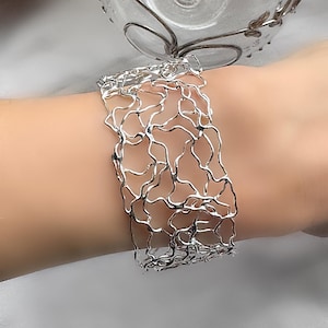 Peut inclure: Un bracelet en argent avec un design délicat et complexe ressemblant à une toile d'araignée ou un filet. Le bracelet est fait de fils fins et entrelacés qui créent un look unique et aérien.