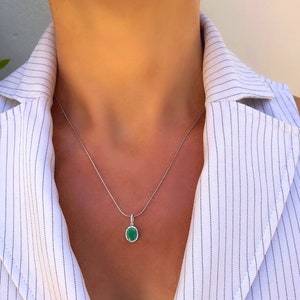 Puede incluir: Un collar de cadena de plata con un colgante ovalado verde engastado en un bisel de plata con peque&ntilde;as piedras transparentes alrededor del borde.