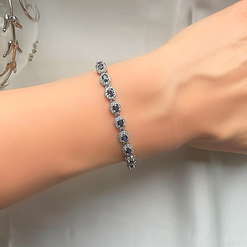 May include: A silver bracelet with a row of oval-shaped blue gemstones surrounded by smaller clear gemstones.