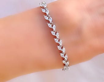 May include: A silver bracelet with a leaf design. The bracelet is adorned with numerous clear, sparkling stones arranged in a delicate pattern. The bracelet is displayed on a wrist.