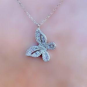 Puede incluir: Collar con colgante de mariposa plateada. El colgante de mariposa est&aacute; incrustado con piedras preciosas claras y brillantes. La cadena del collar es delicada y plateada. Una hermosa joya.