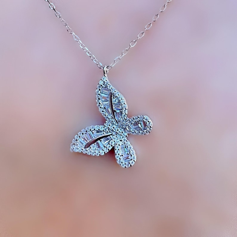 Puede incluir: Collar con colgante de mariposa plateada. El colgante de mariposa est&aacute; incrustado con piedras preciosas claras y brillantes. La cadena del collar es delicada y plateada. Una hermosa joya.