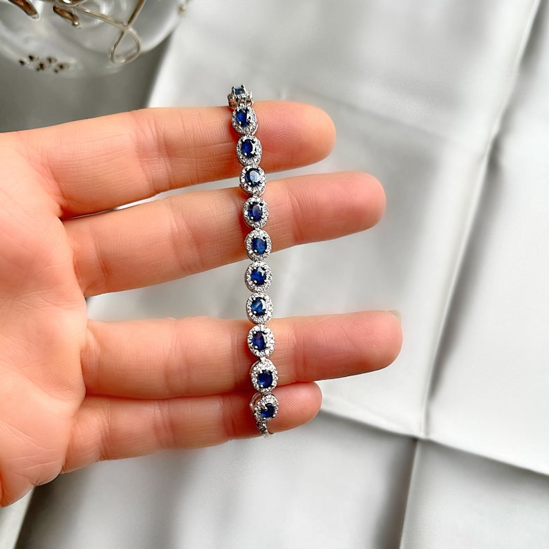 May include: A silver bracelet with a row of oval-shaped blue gemstones surrounded by smaller clear gemstones.