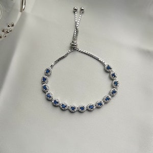 May include: A silver bracelet with a blue gemstone accent. The bracelet has a sliding clasp for adjustable sizing.
