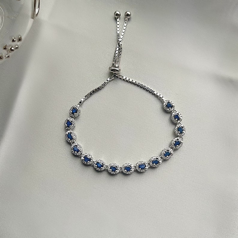 May include: A silver bracelet with a blue gemstone accent. The bracelet has a sliding clasp for adjustable sizing.
