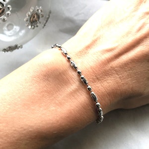 以下が含まれることがあります： 繊細なデザインのシルバーチェーンブレスレット。ブレスレットは、細いチェーンでつながった小さな丸いビーズでできています。