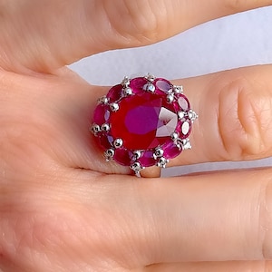 May include: A silver ring featuring a large oval ruby surrounded by smaller rubies.