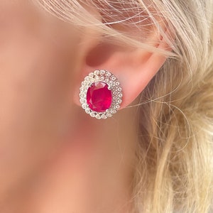 May include: A pair of oval ruby earrings with a halo of small diamonds set in white gold.