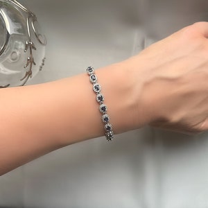 May include: A silver bracelet with a row of oval-shaped blue gemstones surrounded by smaller clear gemstones.