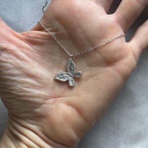 Puede incluir: Un collar de plata con un colgante de mariposa. La mariposa est&aacute; incrustada con peque&ntilde;as piedras brillantes y la cadena es delicada. El collar se muestra sobre un fondo neutro.