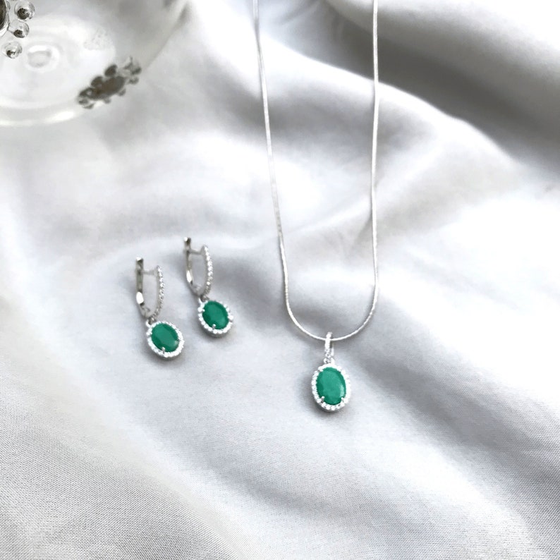 Puede incluir: Un conjunto de collar y pendientes de plata con piedras ovaladas verdes rodeadas por un halo de piedras m&aacute;s peque&ntilde;as.
