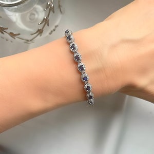 May include: A silver bracelet with a row of oval-shaped blue gemstones surrounded by smaller clear gemstones.