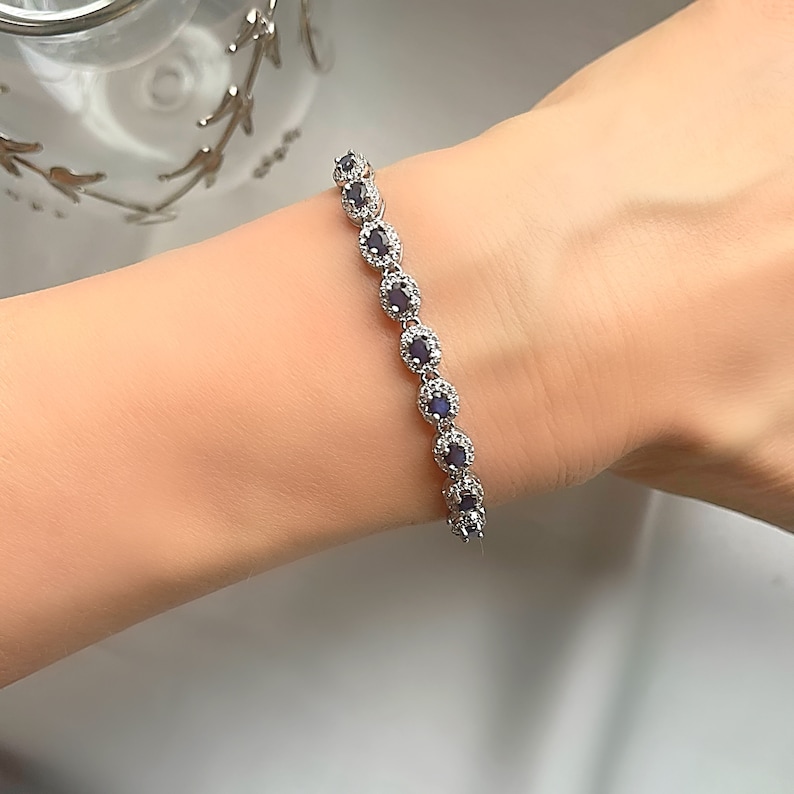 May include: A silver bracelet with a row of oval-shaped blue gemstones surrounded by smaller clear gemstones.