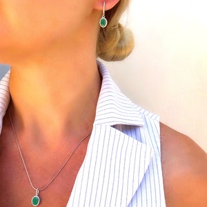 Puede incluir: Un collar y pendientes de plata con piedras preciosas verdes de forma ovalada. El collar tiene una cadena delicada y los pendientes son de estilo colgante.