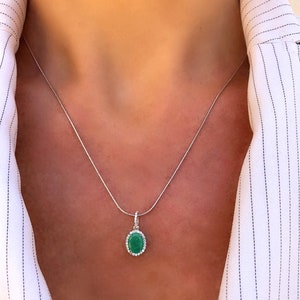 Puede incluir: Un collar de cadena de plata con un colgante que presenta una piedra preciosa verde ovalada grande rodeada por un halo de piedras preciosas blancas m&aacute;s peque&ntilde;as.