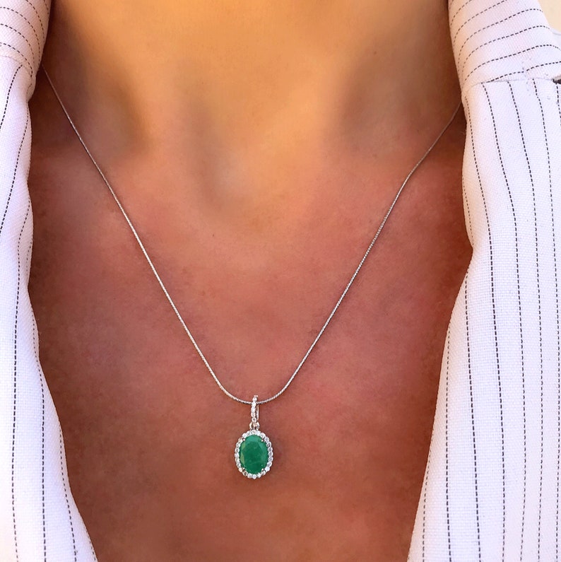 Puede incluir: Un collar de cadena de plata con un colgante que presenta una piedra preciosa verde ovalada grande rodeada por un halo de piedras preciosas blancas m&aacute;s peque&ntilde;as.