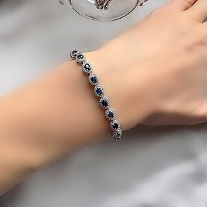 May include: A silver bracelet with a row of oval-shaped blue gemstones surrounded by smaller clear gemstones.
