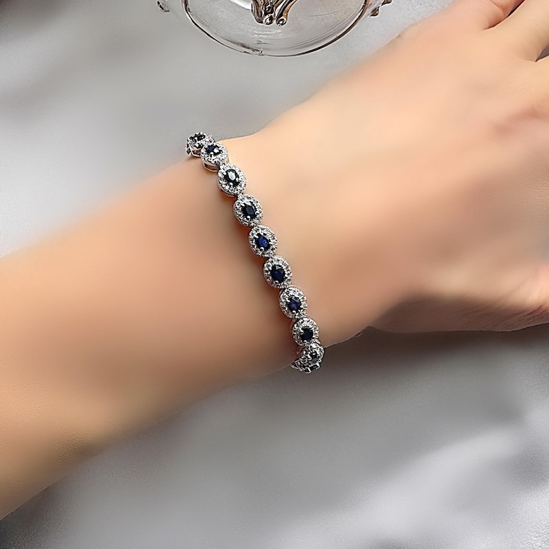 May include: A silver bracelet with a row of oval-shaped blue gemstones surrounded by smaller clear gemstones.