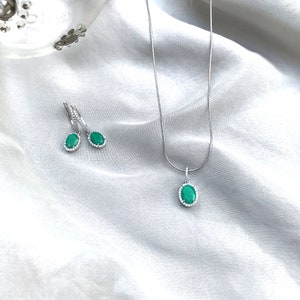 Puede incluir: Un collar y pendientes de plata con piedras preciosas verdes ovaladas rodeadas por un halo de piedras transparentes m&aacute;s peque&ntilde;as.