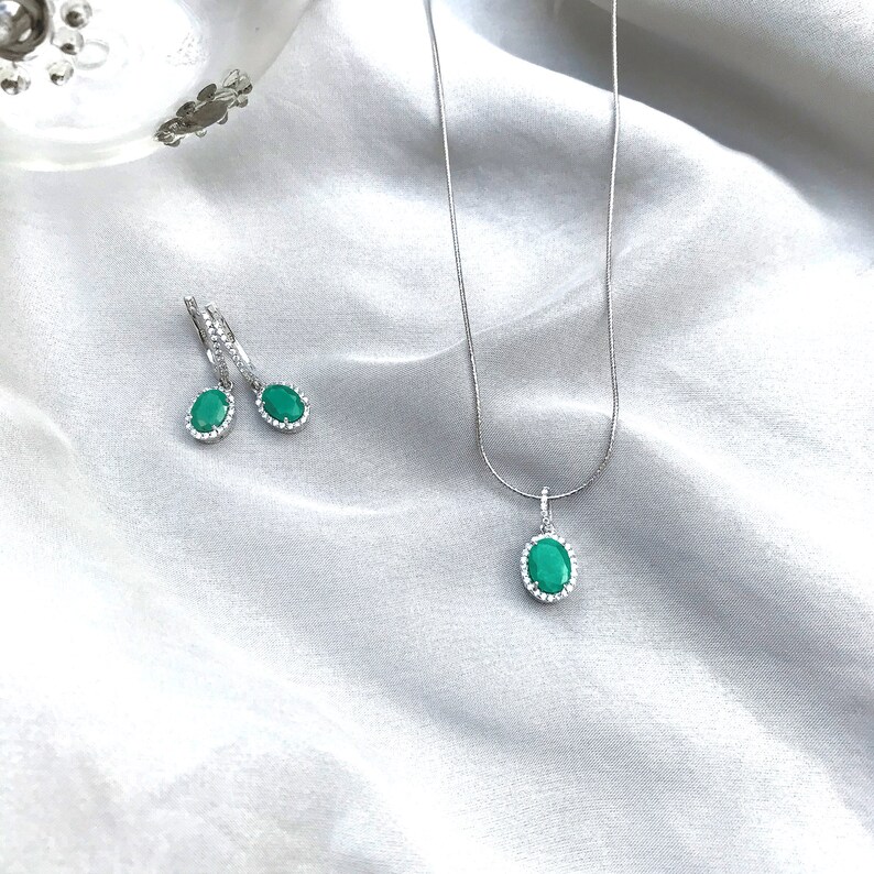 Puede incluir: Un collar y pendientes de plata con piedras preciosas verdes ovaladas rodeadas por un halo de piedras transparentes m&aacute;s peque&ntilde;as.