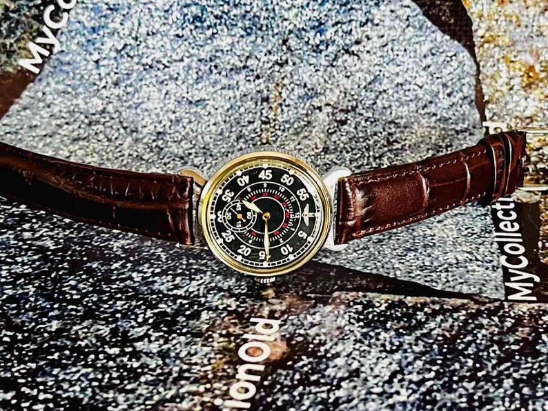 May include: A vintage wristwatch with a black dial and gold-tone case. The watch features a brown leather strap. The dial displays numerals and hands for timekeeping. The watch is a classic accessory.