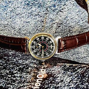 May include: A vintage wristwatch with a black dial and gold-tone case. The watch features a brown leather strap. The dial displays numerals and hands for timekeeping. The watch is a classic accessory.