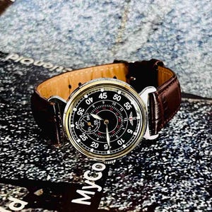 May include: A vintage wristwatch with a black face, white numerals, and a brown leather band. The watch has a silver-colored case and a subdial. The band is dark brown and has a classic design.