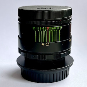 May include: A black camera lens with a green and red aperture scale. The scale reads "16 11 8 4 2 4 8 11 16" and "M 0,5".