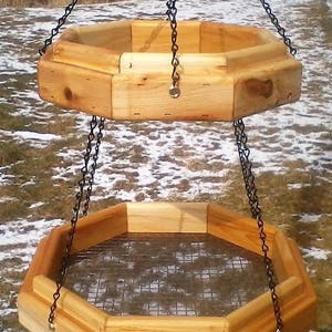 May include: A double-tiered wooden bird feeder with a wire mesh bottom, hanging from black chains.