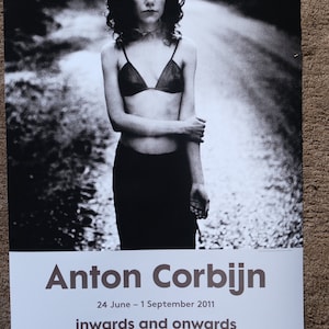 Puede incluir: Una fotografía en blanco y negro de una mujer con un sujetador y una falda negros, de pie en un camino de tierra. El texto "Anton Corbijn" está en la parte superior del póster, y el texto "24 de junio - 1 de septiembre de 2011" está debajo. El texto "inwards and onwards" está debajo de eso. El texto "foam" está en la esquina inferior izquierda, y el texto "delta lloyd" está en la esquina inferior derecha.