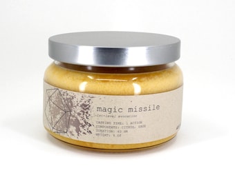May include: A glass jar with a silver lid, filled with a yellow substance. The label reads "magic missile" with details about casting time, components (citrus, sage), duration, and weight (255 g).