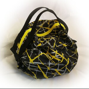 May include: Black and yellow duffel bag with a geometric pattern. The bag has two handles and a zipper closure.