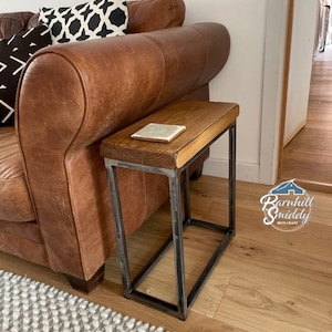 May include: A rustic wooden top side table with a black metal frame. The table is next to a brown leather sofa with black and white patterned throw pillows.