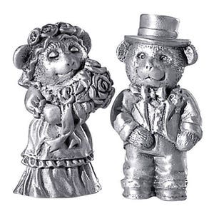 May include: A silver figurine set of a mouse bride and a bear groom. The bride is wearing a white dress with a floral bouquet. The groom is wearing a tuxedo and a top hat.