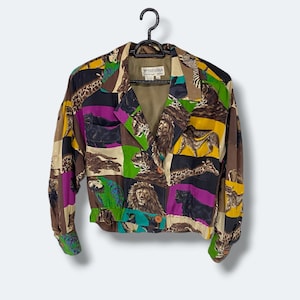 May include: A vintage Trevira fashion jacket with a vibrant animal print. The jacket features a collage of animal illustrations, including lions, zebras, and parrots, in a patchwork design. It has a button closure and elastic cuffs and waist.