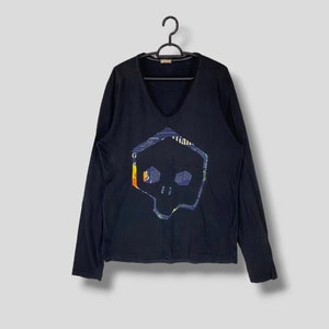 May include: Black long-sleeve shirt with a colorful skull graphic. The skull is made up of a newspaper print.