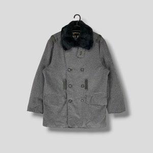 May include: A white ceramic mug with a black handle and the text "But First, Coffee" in a bold, black font. The mug is set against a blurred background, suggesting a cozy setting.