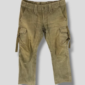 May include: Olive green cargo pants with multiple pockets and straps. The pants have a faded, worn look and a button and zipper closure. The pants are made of a soft, durable material.