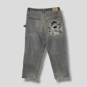 May include: Gray carpenter jeans with a cartoon character patch on the back pocket. The jeans have a frayed hem.