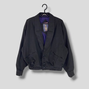 May include: A black jacket with a shawl collar, button closure, and two front pockets. The jacket has a purple lining and is hanging on a black hanger. The jacket appears to be made of a lightweight material.