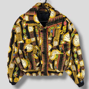May include: A black bomber jacket with a repeating pattern of gold, brown, and white clocks and watch chains. The jacket has a black collar, cuffs, and two front pockets. The jacket is hanging on a black hanger.