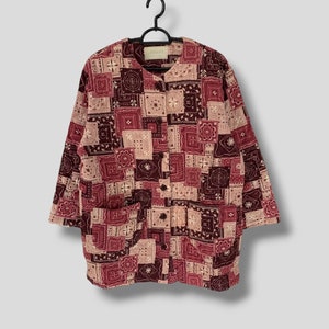 Puede incluir: Una camisa abotonada de manga larga con un diseño de patchwork en tonos burdeos, crema y marrón. La camisa tiene cuello redondo y dos bolsillos delanteros. La marca "URBANS" es visible en el cuello.