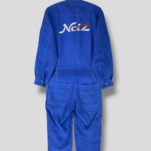 May include: A blue work jumpsuit with the word "Netz" in white lettering on the back. The jumpsuit has white stitching and a zipper closure.