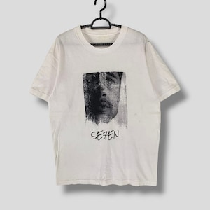 May include: White t-shirt with a black and white graphic of a person's face and the word "SE7EN" printed on the front.