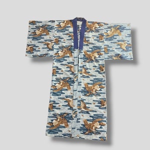 Puede incluir: Un kimono vintage con un patrón repetido de pájaros marrones en vuelo sobre un fondo azul claro con formas onduladas azul oscuro. El kimono tiene un cuello azul oscuro y está hecho de una tela ligera.